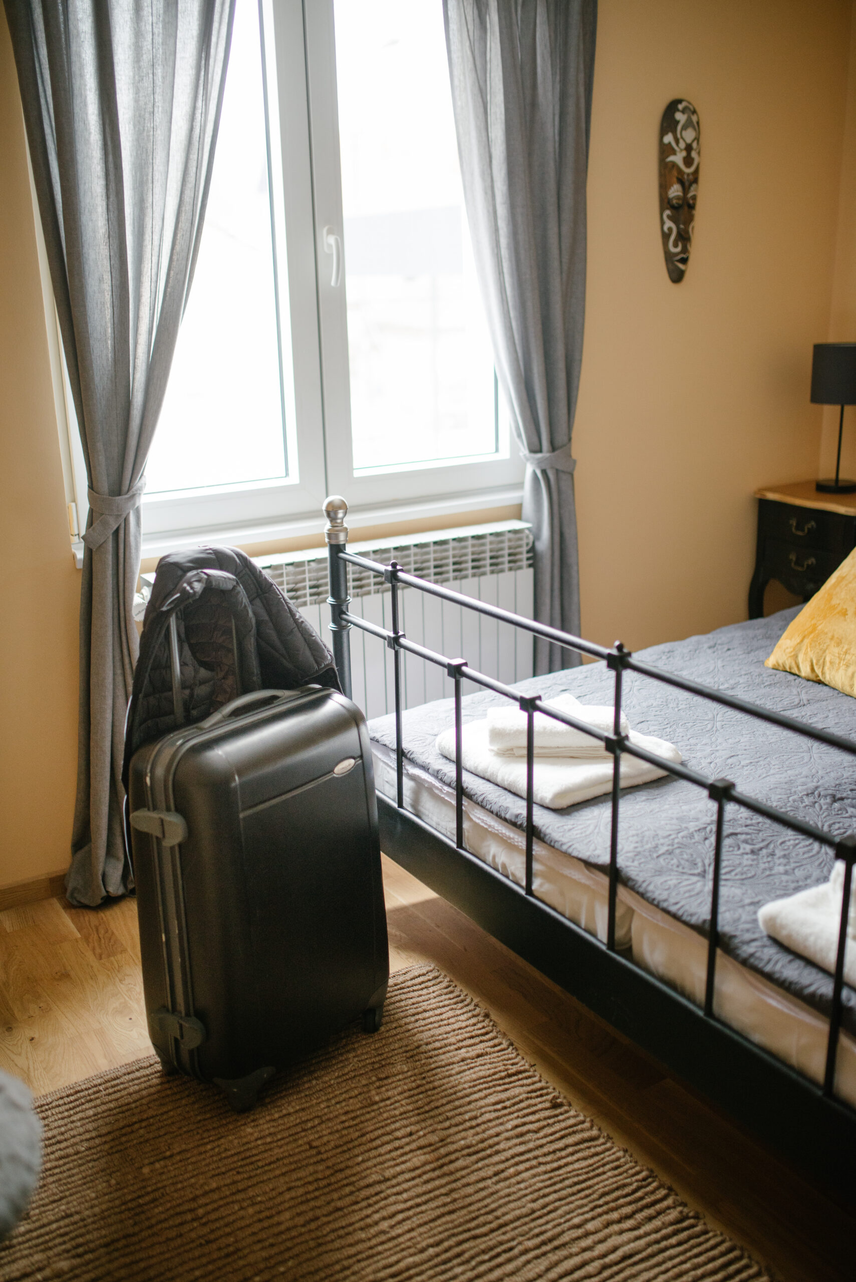 Chambre meublée lumineuse avec lit préparé et valise avant une arrivée