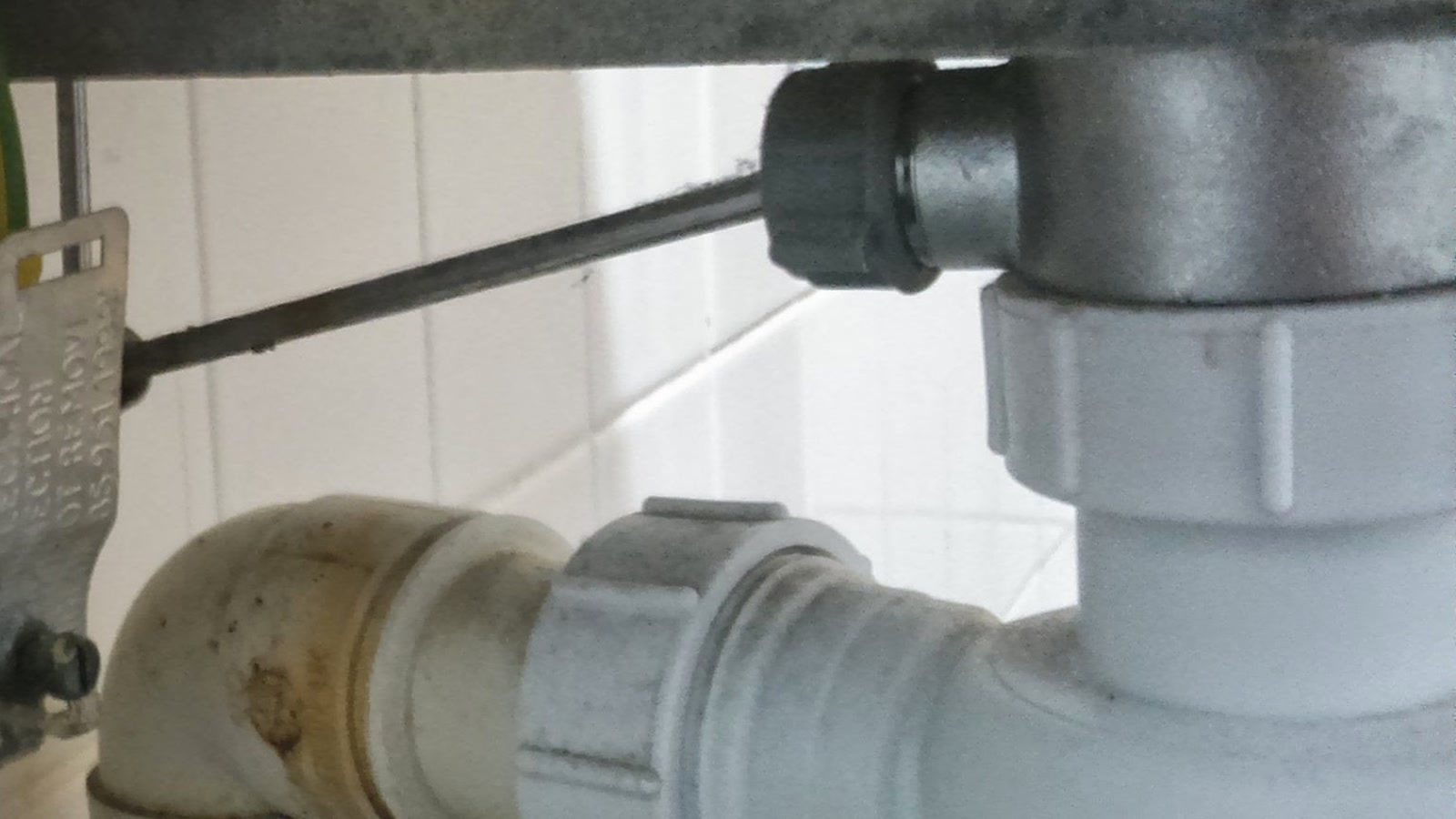 Accès technique sous évier avec siphon et tuyauterie visibles
